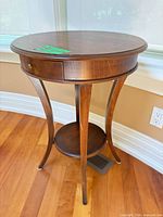 Full view of one round wooden side table showing top, legs, shelf