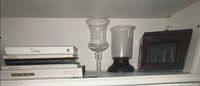 Shelf view showing photo album box, two glass hurricanes, stack of five books