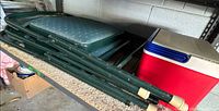 Stack of three folded green padded chairs next to red cooler on shelf