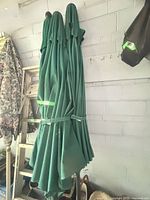 three folded green patio umbrellas propped against wall