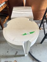 Stack of three round white plastic side tables with square table top resting above