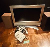 Front view of Sharp TV flanked by two speakers, phone and remotes in front