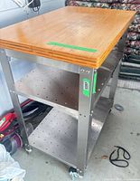Full view of cart showing bamboo top, stainless frame, two perforated shelves, locking casters