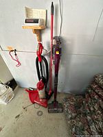 Full view of both vacuums standing side by side with dustpan at base