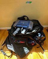 Pile of assorted bags including grey/navy carry bag on top of black backpacks