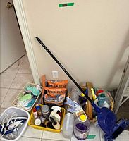 Corner setup showing broom handle, dustpan, iron, cloths bin, Quick Dam bags, totes with cleaners