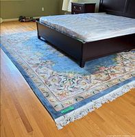 Full view of blue wool area rug under bed showing floral design and fringe