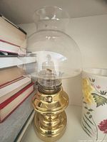 Brass oil lamp between books and floral vessel