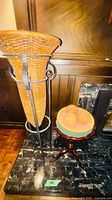Wicker vase in iron stand beside wooden tripod table with bowl and balls