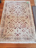 Full view of beige and red wool area rug on hardwood floor