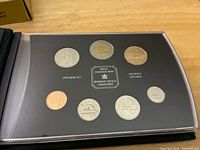 Full view of open presentation case showing all seven coins and interior labelling