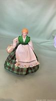 Full view of glass doll standing, showing entire outfit and basket