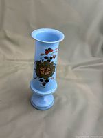 Full view of light blue glass vase showing floral painting and pedestal base
