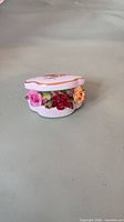 Side view of oval bone china trinket box showing applied roses and gold trim
