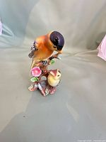 Front view of porcelain figurine showing adult bird, chick, pink flower, leaves