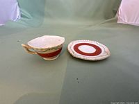Cup and saucer front view showing red band, gold trim, chip on cup rim