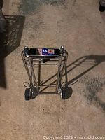 Folded chrome luggage cart on floor showing wheels and frame