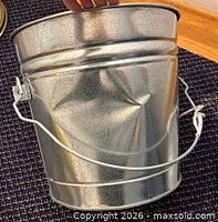 Dented side of galvanized can showing bail handle