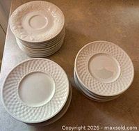 Stacks of white dessert plates and saucers showing two embossed rim patterns