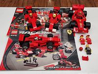 Overview showing three assembled Lego Ferrari F1 cars, two instruction manuals (sets 8375 and 8144), minifigure drivers and accessories