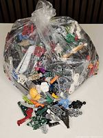 Large clear bag filled with assorted Lego Bionicle parts with some pieces spread out in front