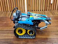Left side view of partially assembled tracked stunt racer showing blue body panels, yellow wheel hubs and rubber tracks