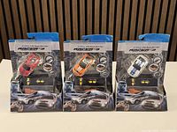 Front view of three sealed Racer-3 1/64 scale RC car packages showing colour variants and included controllers