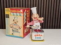 Tin Chef Cook toy beside original box, front view