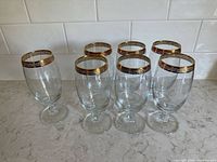 Front view of seven glass goblets showing gold rims