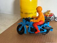 Blue BMW motorcycle toy with orange rider on brown surface, yellow Kinder capsule and small red motorcycle visible