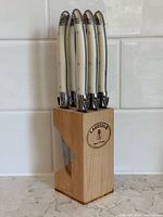 Front view of wooden block holding six white-handle steak knives