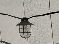 Close view of single caged glass patio light on wire
