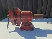 Left side view of red Ohio Forge 5" bench vise showing swivel base and handle