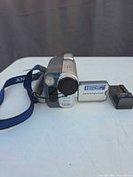 Side view of Sony Handycam with blue hand strap, lens cap and separate battery charger