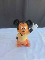 Front view of vinyl Mickey Mouse coin bank showing waving pose and orange sack