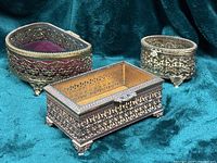 Three gold-tone filigree jewelry caskets on teal fabric