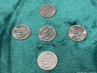 Five Eisenhower dollars laid out on green fabric