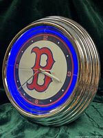 Front angled view of clock showing chrome ribbed bezel, blue neon ring, dial details