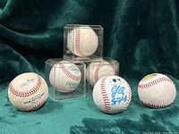 Group shot of five baseballs showing three in display cubes and two loose, autographs and logos partially visible