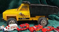 Side view of Tonka dump truck with six Hot Wheels vehicles lined in front