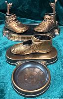 Pair of bronzed lace-up shoes on decorative platform, single shoe stand in foreground