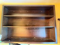 Front view of dark wood wall shelf showing three shelves and mounting holes