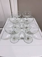 Six clear coupe glasses on surface, front angle