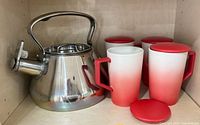 Kettle and four mugs with lids inside cabinet
