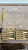 Full lot showing glass plate, porcelain server, two boxes of knives, tape for scale