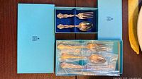 Birks blue boxes open showing three flatware pieces, two still in plastic sleeves