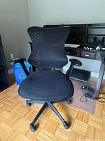Front view of black mid-back office chair showing mesh-style back, padded seat and armrests