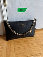 Front view of black Coach pebbled leather bag showing gold chain strap and zipper
