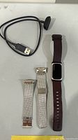 All items laid out: smartwatch with brown leather band, two silver mesh bands, black USB charger