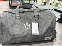 Front view of gray Herschel duffel displaying Toronto Maple Leafs logo and hang tag